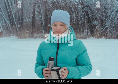 15-year-old girl walking in  winter forest holds thermos and mug of hot tea. Picnic in the snow. Stock Photo