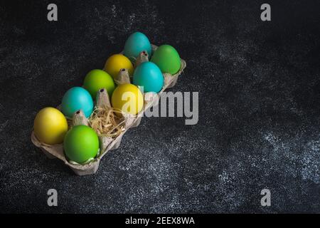 Colorful painted easter eggs in egg carton decorated with shavings on black background. Copy space Stock Photo