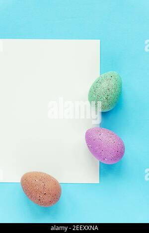 Three painted eggs and blank sheet on blue background, top view, flat lay. Easter concept. Stock Photo
