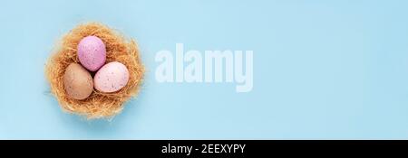 A nest with painted easter eggs on blue background. Easter concept. Top view, flat lay, copy space. Stock Photo