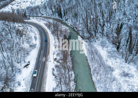 Aerial view of road and river in mountain gorge in snowy day, winter travel and car journey exploration concept. Stock Photo
