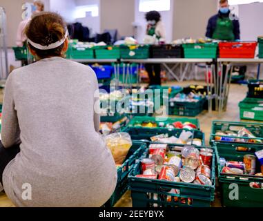 Food bank volunteer at Trussell Trust foodbank crouched beside crates of donated food with other volunteers sorting and collecting food. London, UK Stock Photo