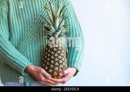 Woman in green sweater holding pineapple. Close up. Stock Photo
