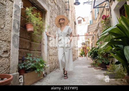 Beautiful blonde young female traveler wearing straw sun hat sightseeing and enjoying summer vacation in an old traditional costal town at Adriatic Stock Photo
