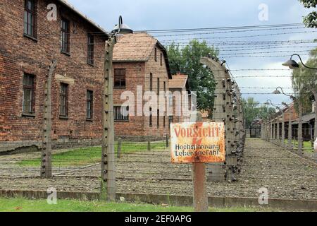 Barbed wire and barracks of Auschwitz concentration camp, sign in German reads 'Attention! high voltage, risk of death', Oswiecim, Poland Stock Photo