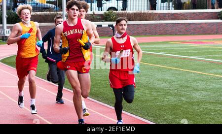 Mineola, New York, USA - 16 January 2021: Front view of high school blys running in a relay race wearing gloves and face masks gaiters becasue of the Stock Photo