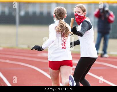 Hicksville, New York, USA - 17 January 2021: Girls exchanging the baton during a relay running race wearing face mask gaiters because of the coronavir Stock Photo