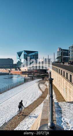 Cyclist cycling along Spree river. Berlin main railway station Hauptbahnhof, Hbf. Snow on riverside, ice on the river. Modern architecture in Germany. Stock Photo