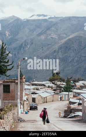 PINCHOLLO, COLCA VALLEY, PERU - JANUARY 20, 2018: A peruvian girl walks with a bag across the street with mountain. in the background in the small vil Stock Photo