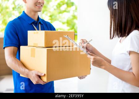 Woman signing document, receiving parcel box from delivery man - courier service concept Stock Photo