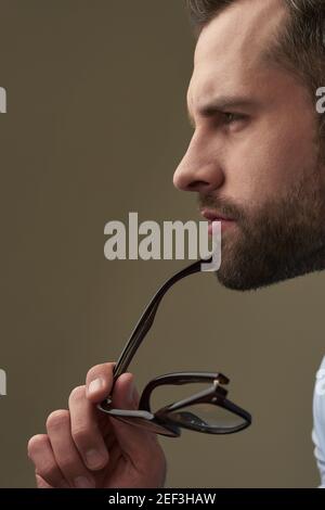 Serious Caucasian man holding spectacles and looking away. Portrait on the brown background Stock Photo
