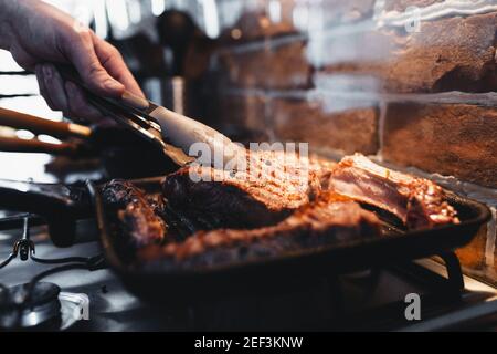 Hand turns steak with tongs during preparation on the grill pan with seasonings. High quality photo Stock Photo