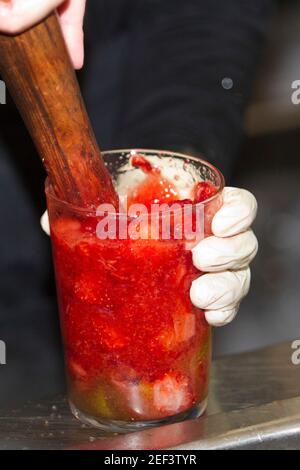 bartender with latex gloves crushing natural strawberry in glass with ice Stock Photo