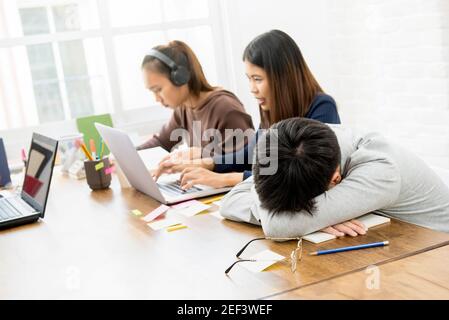 Group of students in co-working space with one student sleeping at the table Stock Photo