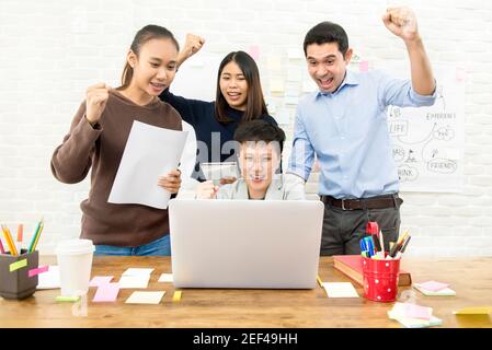 Group of university students raising their fists celebrating while looking at laptop computer in study room - win and success concepts Stock Photo