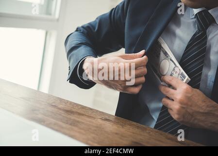 Businessman putting money, Japanese  yen banknotes, into his suit pocket - bribery and corruption concept Stock Photo