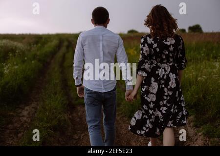 Back view of the couple holds hands and walks in the meadow  Stock Photo