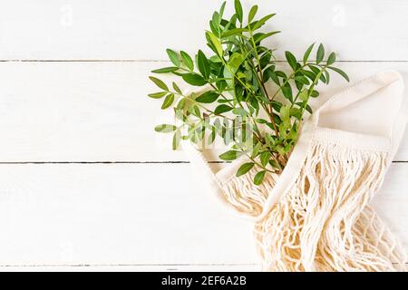 Top view of bunch of green branches in cotton mesh bag with copy space. Eco friendly backdrop. Light and airy fat lay. Stock Photo