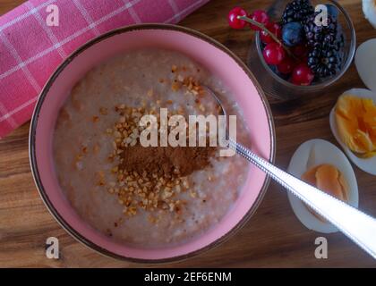 A bowl of fresh cooked porridge with roasted almonds and cinnamon served with a glass of fresh berries and boiled eggs Stock Photo