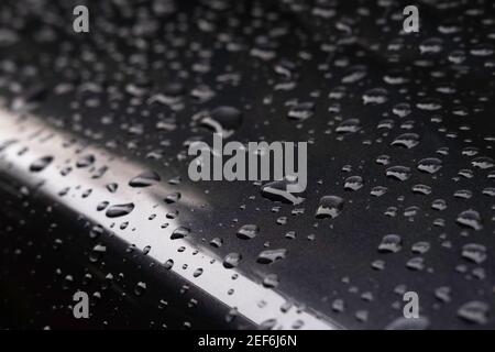 Waterdrops on a darkgray metallic car. Focus on the large drop in front Stock Photo