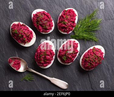 Stuffed eggs with beetroot with cream cheese, garlic and spicy herbs on a black slate background, top view. delicious homemade food Stock Photo
