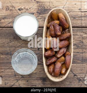 Dried dates fruits on a branch, a glasses of water and milk on a wooden table. Traditional fast breaking, Muslims evening meal during holy Ramadan Stock Photo