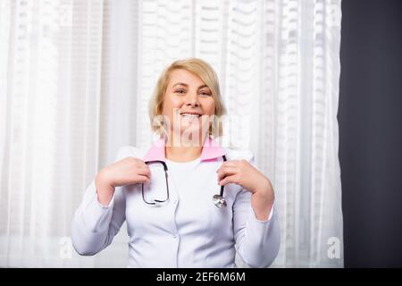 Experienced medical professional with stethoscope. Senior caucasian female doctor smiling cute in camera posing in the medical office Stock Photo