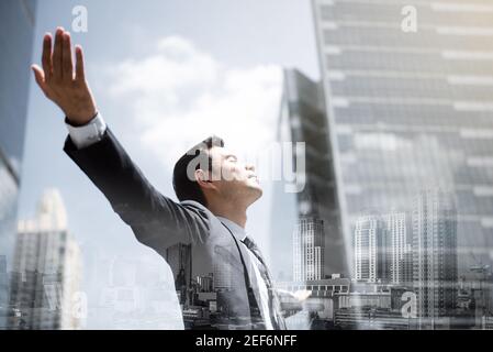 Businessman in the city raising his arms, open palms, with face looking up - empowering, success and freedom concepts, double exposure effect Stock Photo