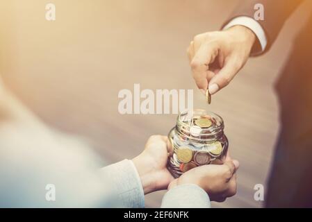 Businessman hand putting money (coin) in the glass jar held by a woman, vintage tone effect Stock Photo