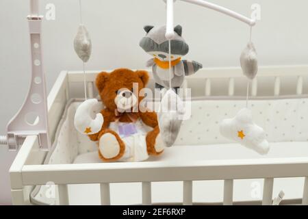 Pcture of a brown teddy bear with diaper on sitting in baby bed Stock Photo