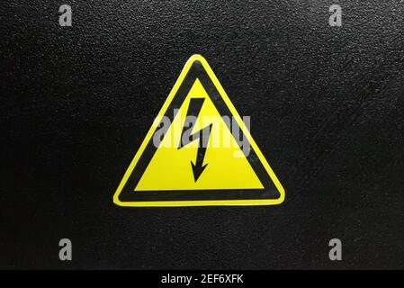 Close up yellow high voltage sign on black wall Stock Photo