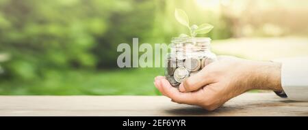Plant growing from money (coins) in the glass jar held by a man's hands  - business and financial metaphor concept, web banner with copy space Stock Photo