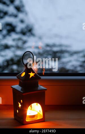Ceramic lantern with a candle by the window. Winter landscape is visible in the distance. Stock Photo