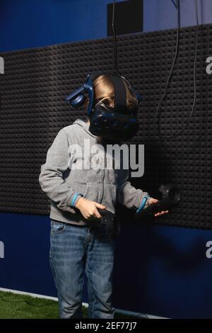 6 year old boy in virtual reality helmet is learning how to control game using controllers. Stock Photo