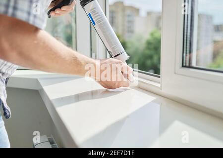 A worker with a construction syringe fills seam between sill and window with silicone sealant Stock Photo