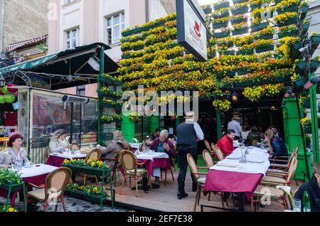 Flowers in pots on historic place Skadarlija with trees, cafes, cobbled lanes and alleys in downtown. Belgrade street with bars and restaurants. Stock Photo