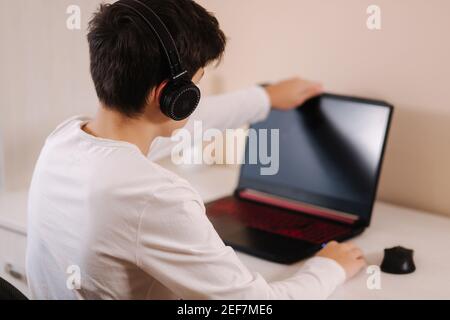 Young boy in headphones open laptop and start playing games. Handsome teenage boy steamer Stock Photo