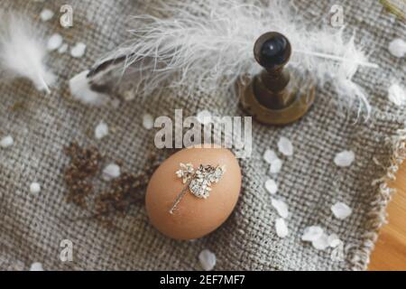 Easter egg decorated with dry flower petals on background of rustic linen napkin,candle and feather. Creative natural eco friendly decor of easter egg Stock Photo