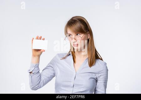 Young businesswoman showing a empty white blank business card. Business woman wearing ultimate gray shirt and glasses looking serious at card on gray Stock Photo