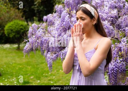 Girl with nose allergy sneezing. Polen illnes symptom concept. Woman allergic to blossom during spring blooming tree outdoor. Stock Photo