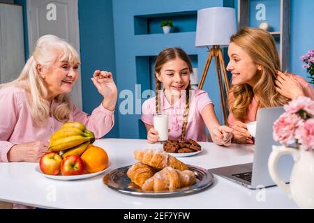 Happy family doing breakfast in the morning at home - Grandmother, daughter and nephew eating at kitchen table at home, domestic life moments Stock Photo