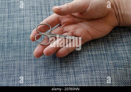 Manicure scissors lie in the open palm of an adult male. The hand rests on a blue surface. Close-up. Selective focus. Stock Photo