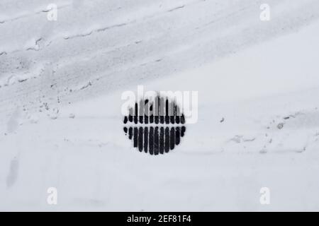 Top view of frozen and snow-covered storm drainage grate, car tracks and footprints in the snow. Random elements on the street in winter. Stock Photo