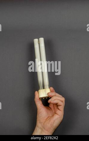 A hand holds a burnt-out  fluorescent lamp on a gray background. An old electric lamp for a table lamp. Side view. Stock Photo