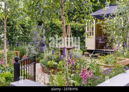 A small English country cottage garden with Summerhouse Shepherds Hut in gravel garden  working from home office  raised bed flower border obelisk UK Stock Photo