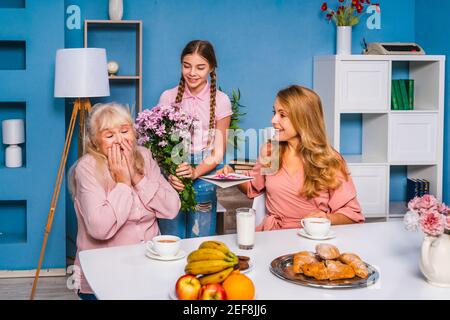 Happy family doing breakfast in the morning at home and celebrating birthtday - Grandmother, daughter and nephew eating at kitchen table at home, dome Stock Photo