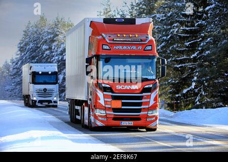 Two freight transport trucks haul goods on wintery Highway 52, red Scania R500 Haukkala and FNA trailer in the front. Salo, Finland. February 11, 2021 Stock Photo