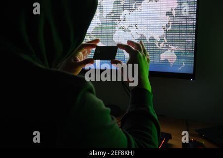 Hacker holding a credit card front of a computer for organizing massive data breach attack around the world. Cyber criminal concept. Stock Photo