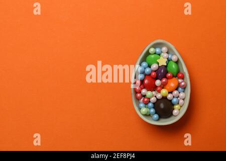 Half of chocolate egg with candies on orange background Stock Photo