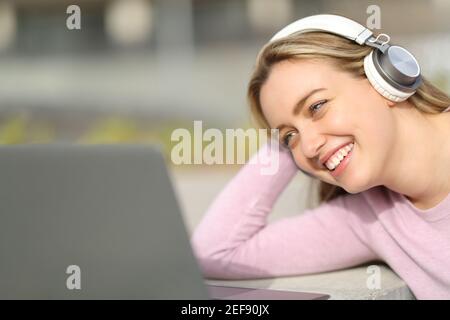 Happy teen wearing headphones watching and listening media on laptop in a park Stock Photo